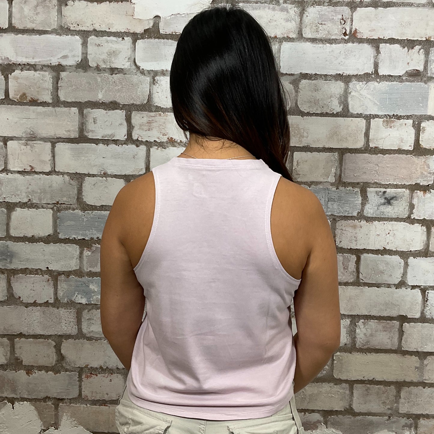 Person wearing a light pink sleeveless top against a brick wall. 'Feeling Berry Good' graphic tshirt. Baby pink graphic tshirt upcycled by unwantees, tank top upcycled by unwantees, atleisurewear recycled clothing, sustainable clothing brand