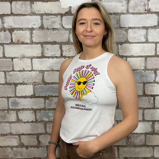 Person wearing a white sleeveless shirt with a colorful graphic design against a brick wall. v