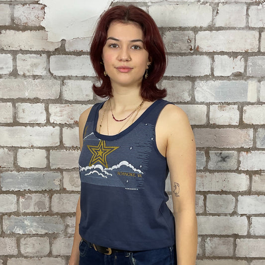 Woman wearing a blue tank top with a star design against a brick wall. One-of-a-kind Roanoke VA Mystical Night Sky graphic Scoop Neck Unwantee tank top front view, upcycled, sustainable, made in Britain