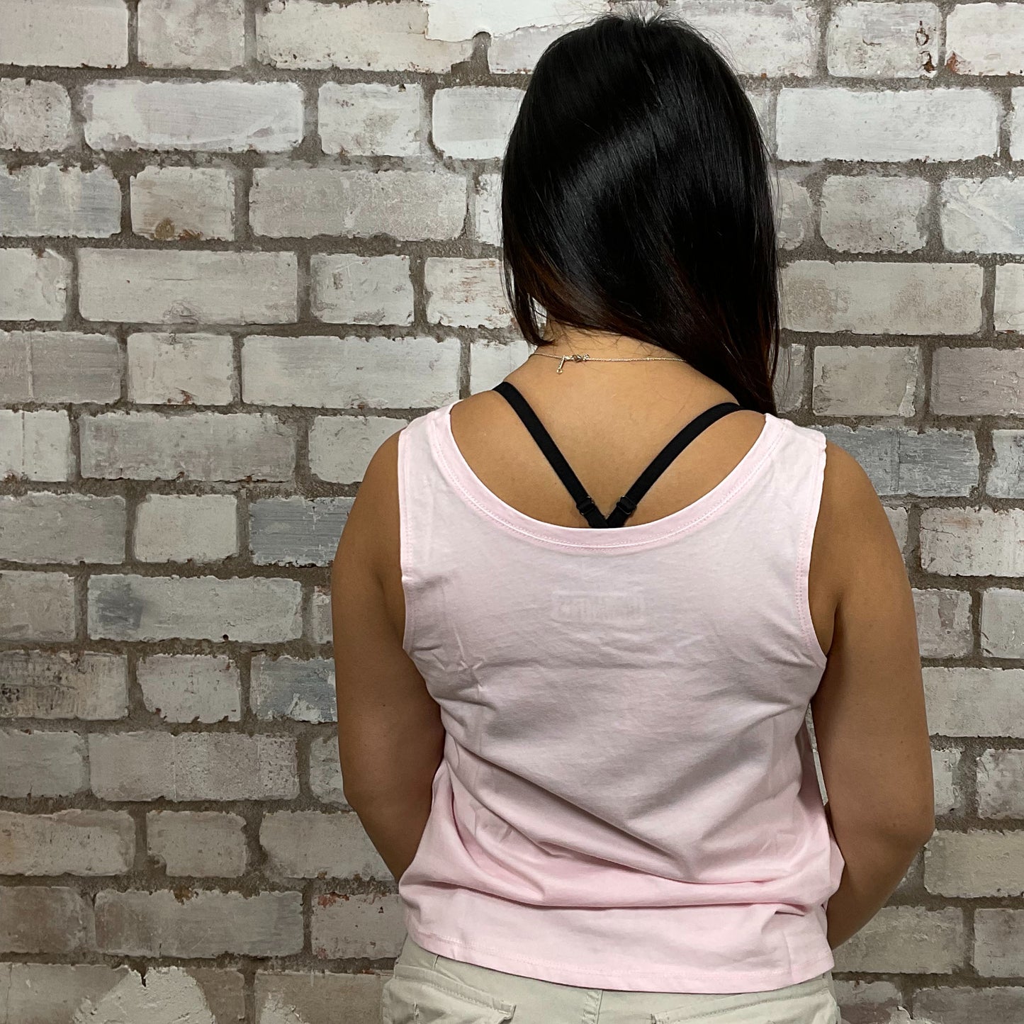 Person wearing a light pink tank top with thin straps against a brick wall. One-of-a-kind Rainbow Flower graphic Scoop Neck Unwantee tank top front view, upcycled, sustainable, made in Britain