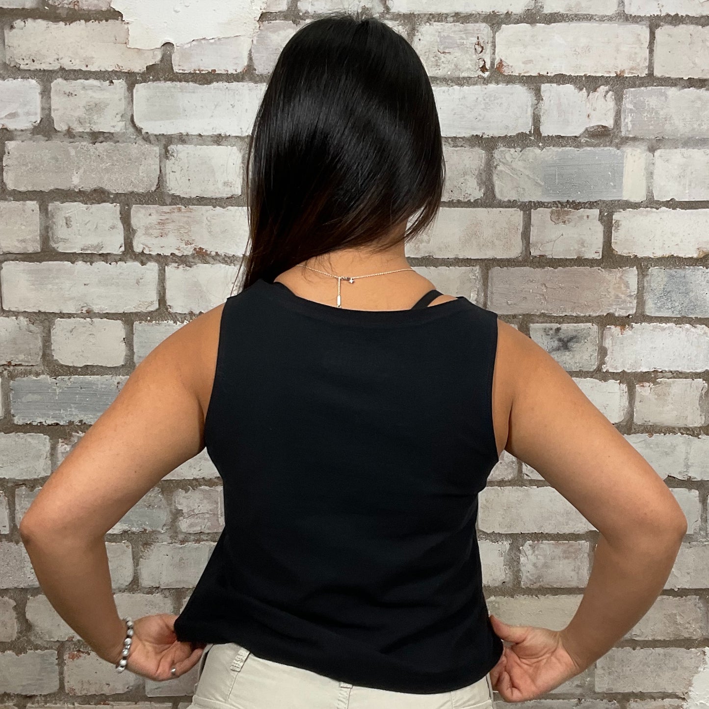 Person wearing a black sleeveless top against a brick wall. v