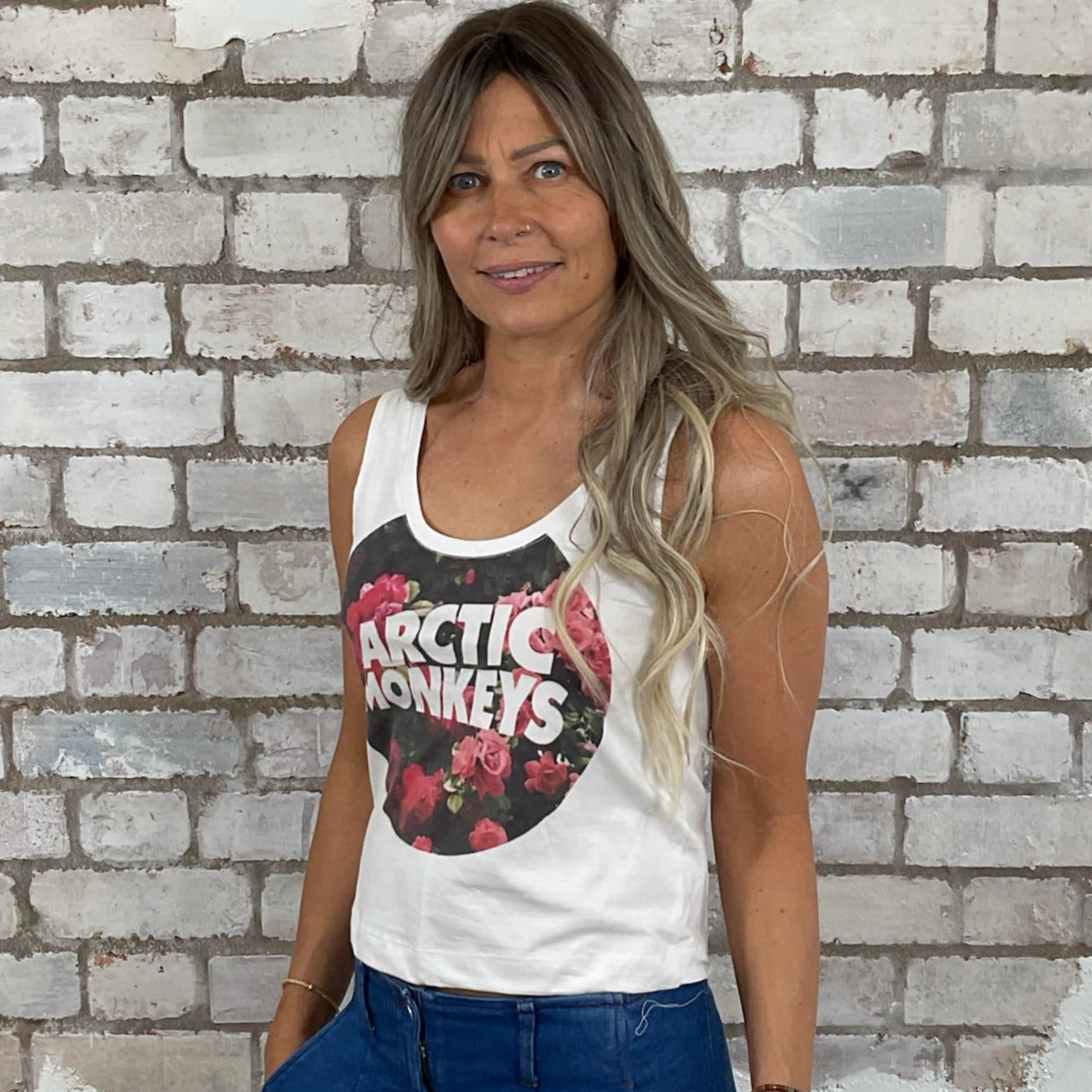 Woman wearing a tank top with a graphic design in front of a textured brick wall. Arctic Monkeys Floral Tank Top, Vibrant coloured top by Arctic Monkeys Up Cycled recycled by Unwantees