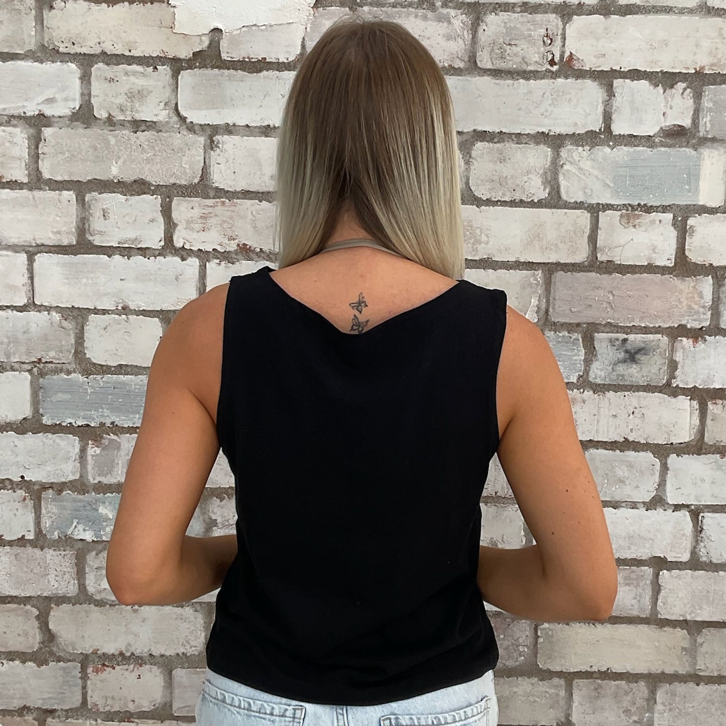 Person wearing a black sleeveless top against a brick wall.