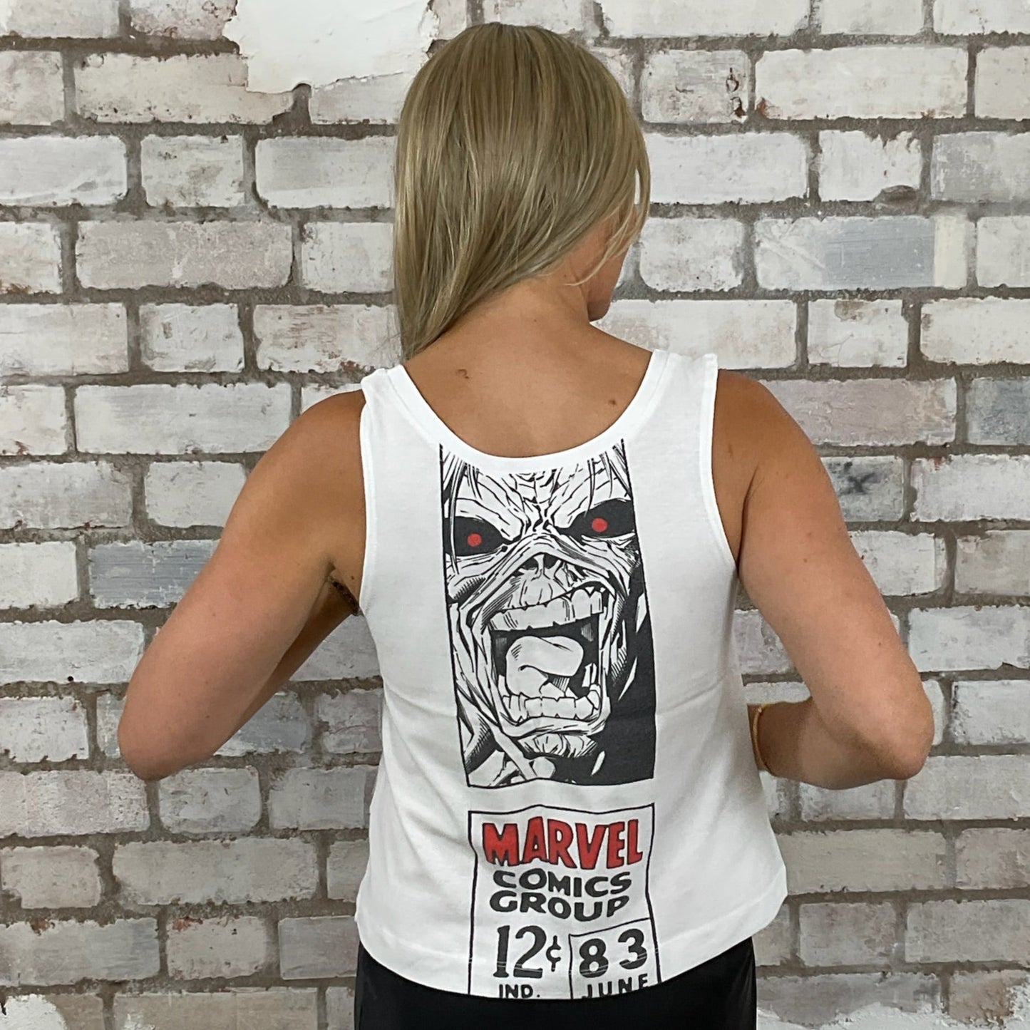 Person wearing a white tank top with a Marvel Comics graphic design against a textured brick wall. Iron Maiden Zombie meets marvel tank top, Unique vest top Iron maiden, Marvel vest top, unwantees up cycle, recycled clothing by Unwantees, sustainable fashion, tshirt rework