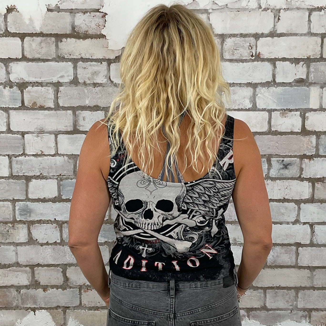 Person wearing a tank top with a skull design against a textured white brick wall.