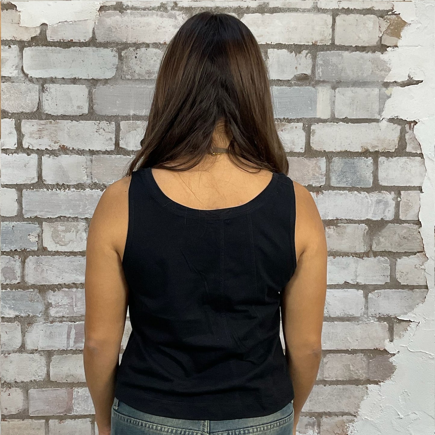Person wearing a black tank top against a textured brick wall, vest upcycled from unwanted clothing, recycled in the UK by unwantees