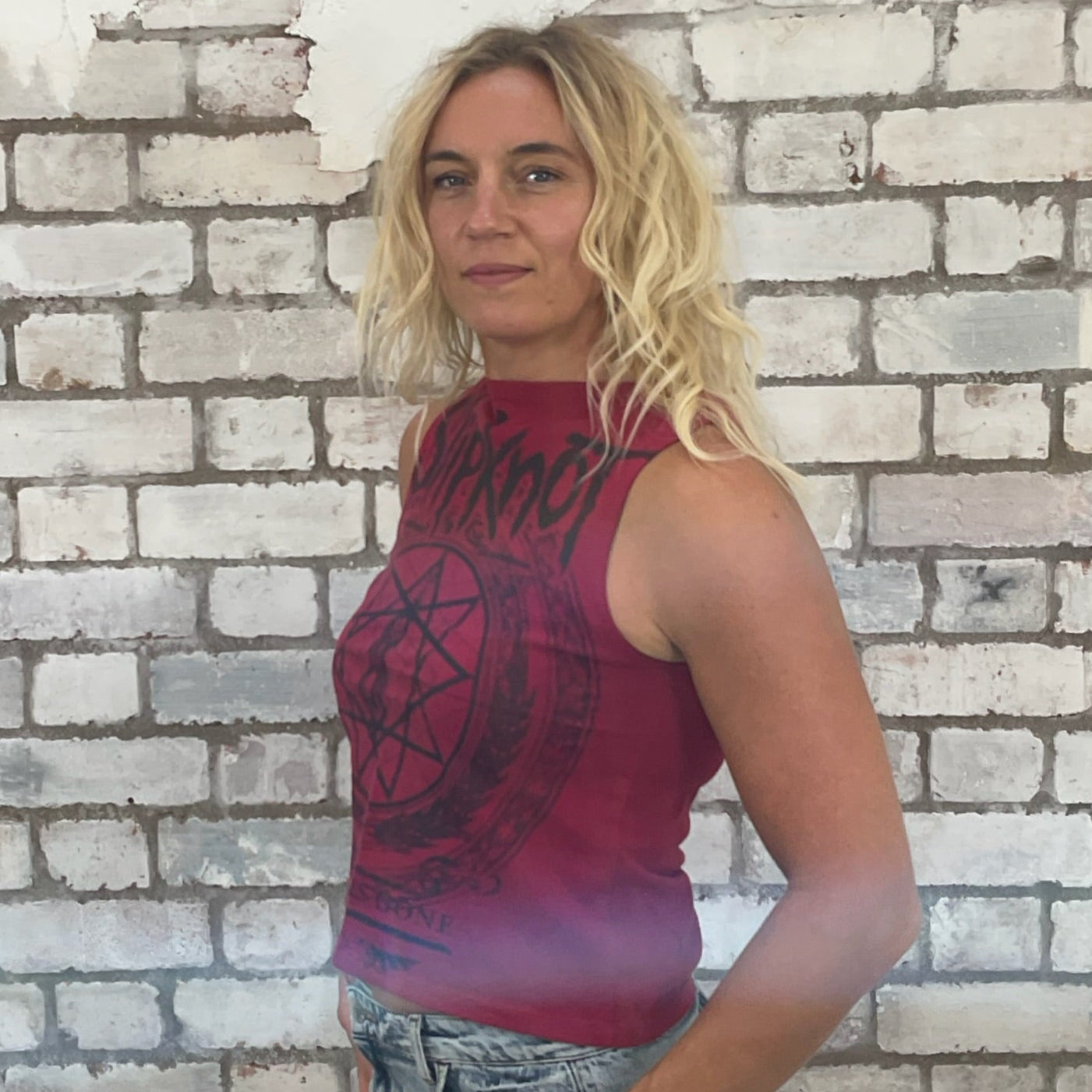 Woman wearing a red tank top with a black design against a brick wall. Slipknot, Deep Red Tank Top, Heavy Metal Vest, Slipknot merch, Up cycle by Unwantees, front and back printed top by Slipknot nonagram print