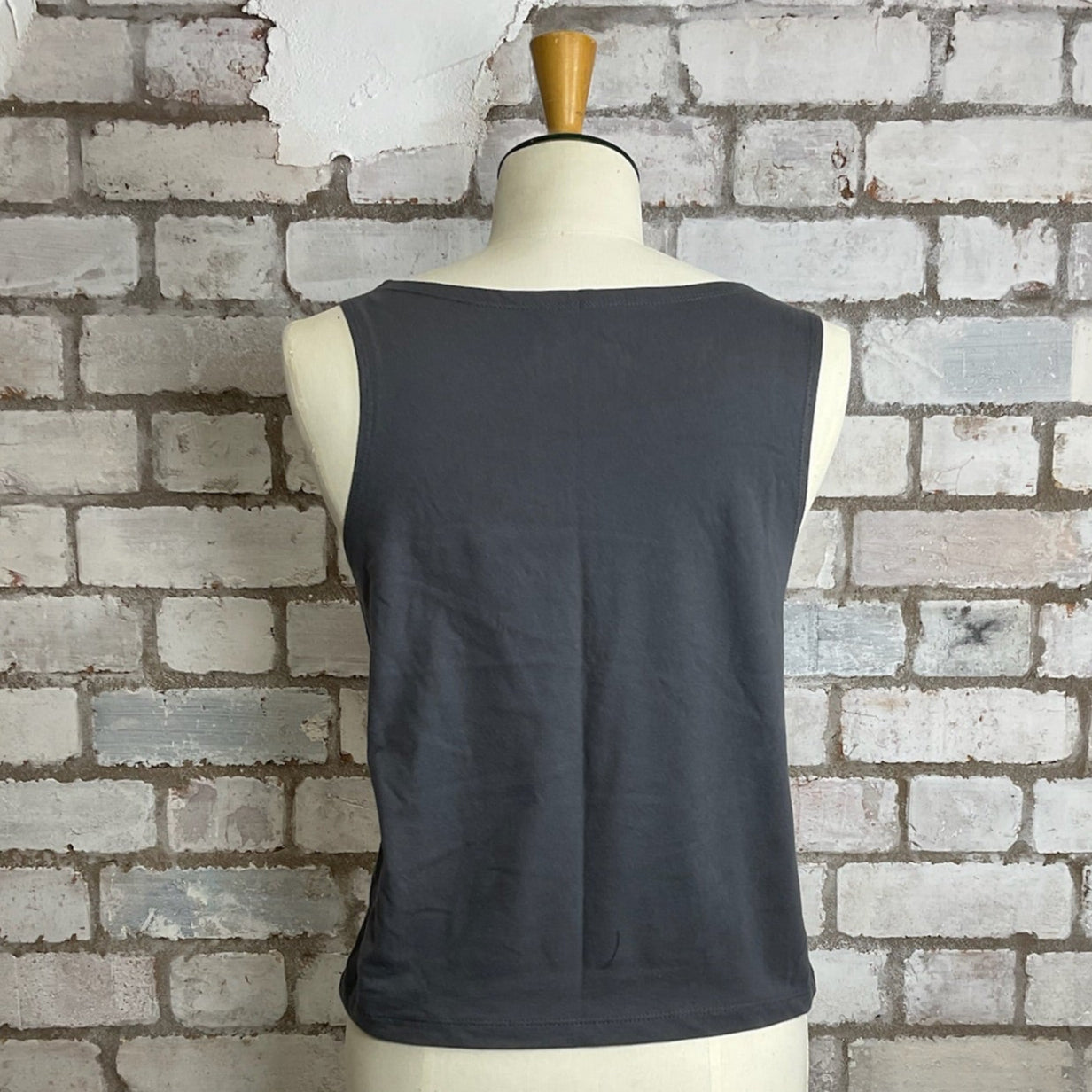 Black sleeveless top on a mannequin against a textured brick wall.