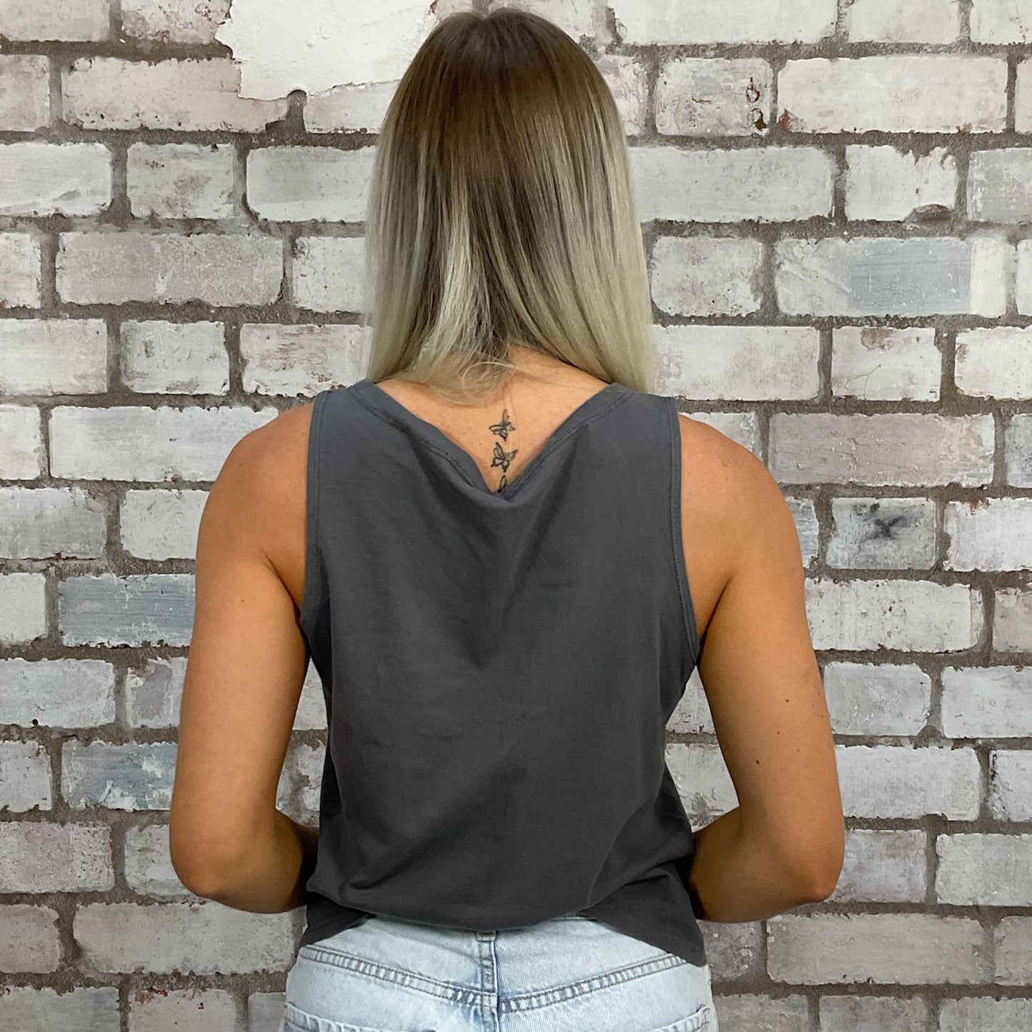 Person wearing a gray tank top with a brick wall background