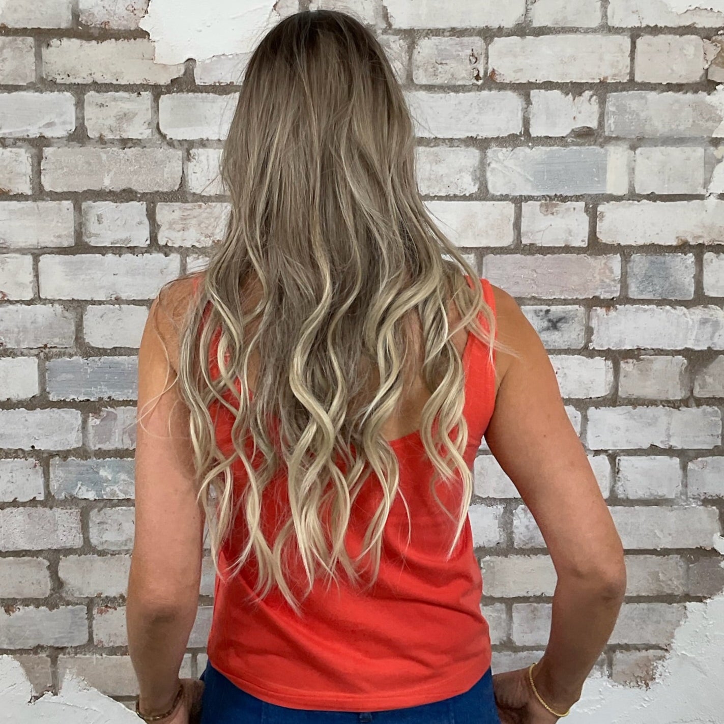 Woman with long blonde hair wearing a red top and blue jeans standing in front of a white brick wall. Woman wearing a colorful tank top with a scenic nature design against a white brick wall. Unwantees Virginia Graphic print tank top, Virginia State Vest, Up Cycled fashion by Unwantees