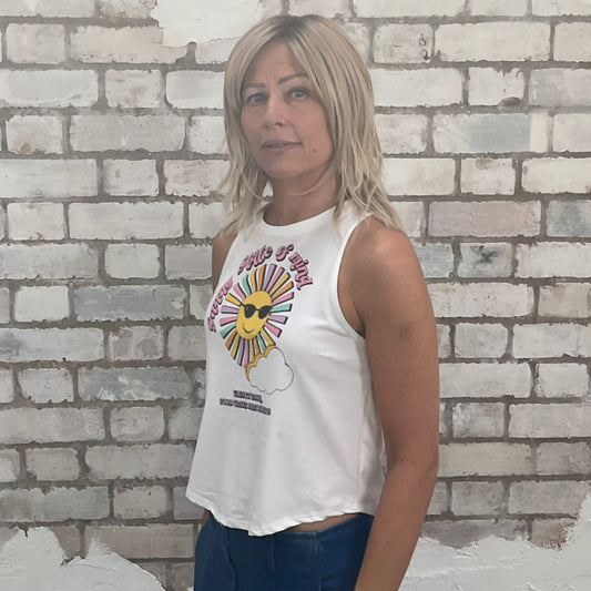 Woman wearing a white sleeveless top with a colorful design against a textured brick wall. recycled fashion by Unwantees