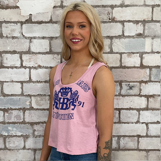 Woman wearing a pink tank top with blue text against a white brick wall. preloved tshirt recycled fashion by unwantees, upcycled in the uk, sustainable fashion, slow fashion, eco conscious fashion