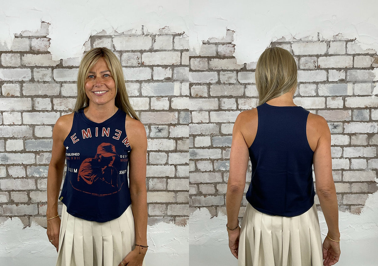 Woman wearing a navy Eminem Unwantee racerback tank top, front and back view, standing against a white brick wall