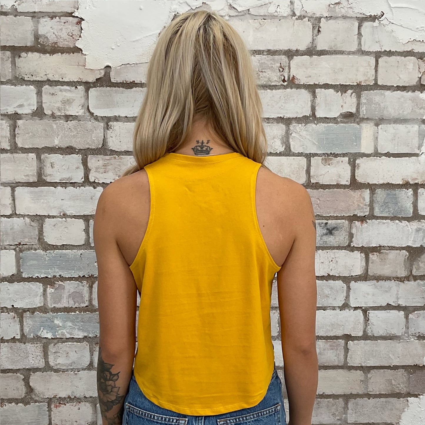 Person wearing a yellow tank top against a brick wall. sustainable fashion, environmentally friendly wardrobe
organic cotton alternatives
waste-to-wear fashion
conscious consumer fashion