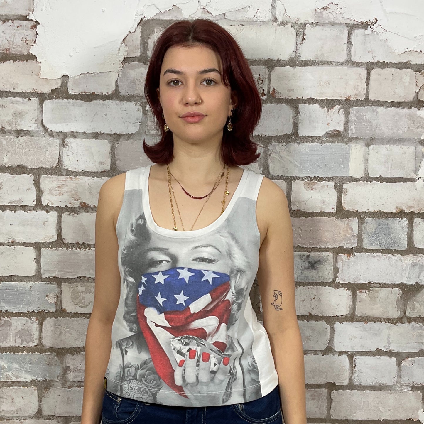 Woman wearing a tank top with a graphic design against a brick wall.  Marilyn Munroe Diamonds and USA Flag print tshirt upcycled by unwantees, atgleisurewear recycled clothing, sustainable clothing brand