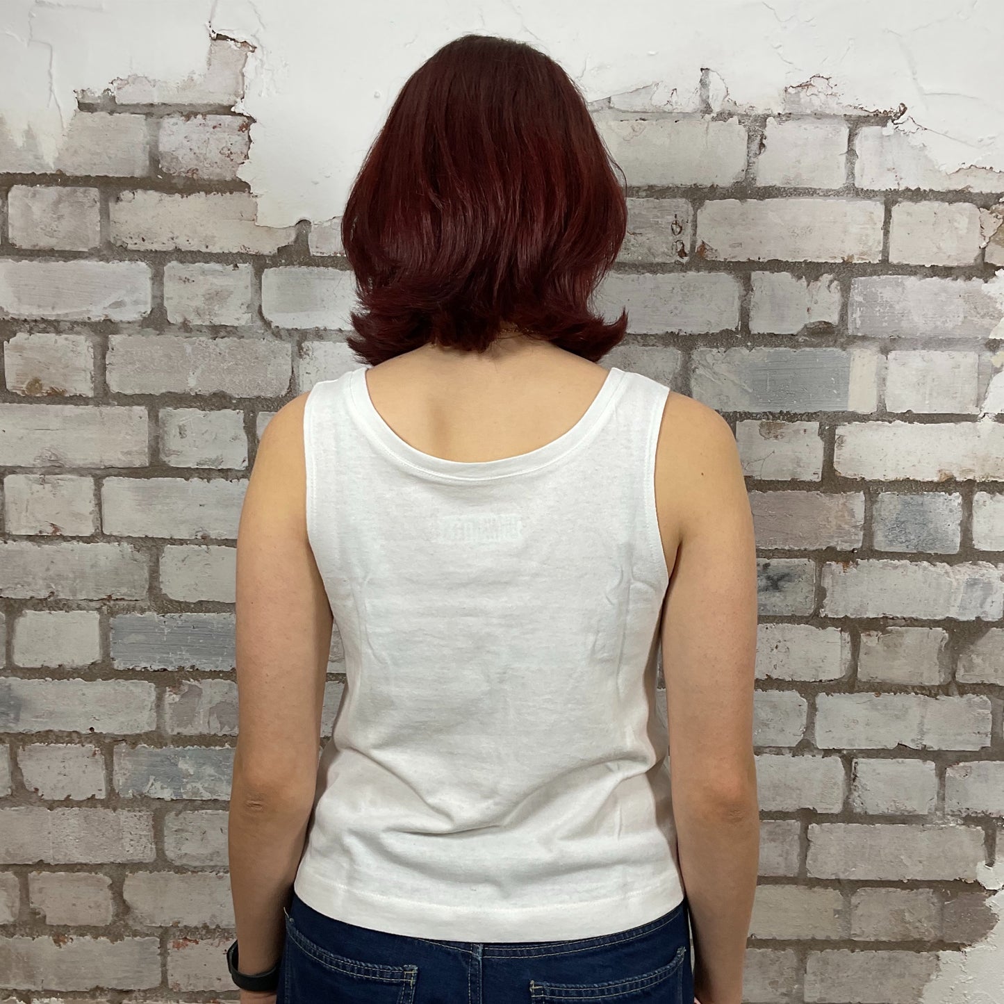 Person wearing a white tank top and blue jeans standing against a textured brick wall.  Marilyn Munroe Diamonds and USA Flag print tshirt upcycled by unwantees, atgleisurewear recycled clothing, sustainable clothing brand