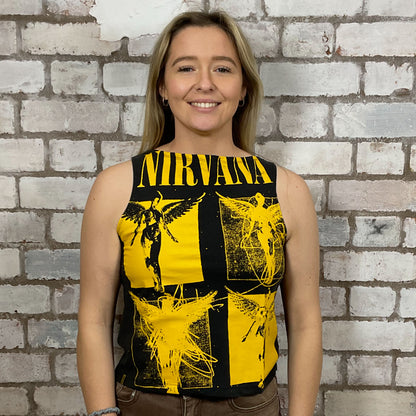 Person wearing a sleeveless shirt with yellow and black designs against a brick wall.  One-of-a-kind Nirvana Acid Face Yellow Print graphic Slash Neck Unwantee tank top close-up view, upcycled, sustainable, made in Britain