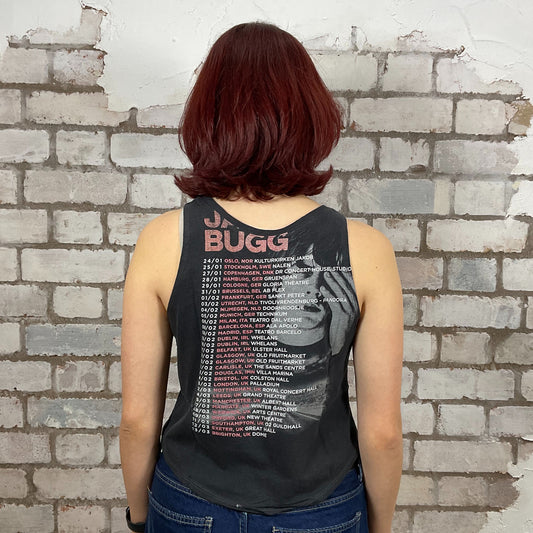 Person wearing a black tank top with text and graphics, standing against a textured brick wall.  Jake Bugg Hearts that Strain Tour Tshirt upcycled by unwantees, recycled tank tops made in the uk