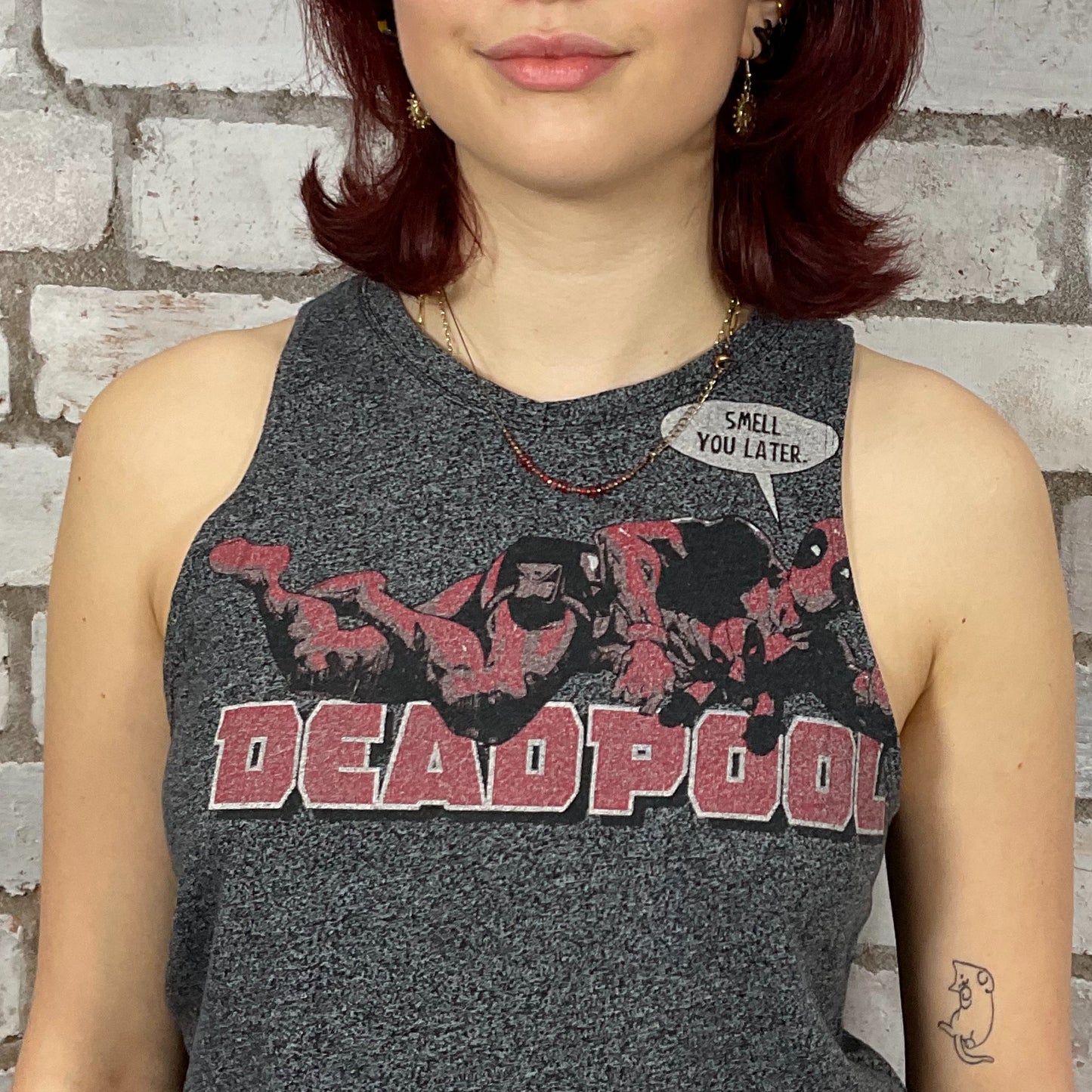 Person wearing a gray tank top with Deadpool graphic and text against a brick wall.  Dark Grey marl Deadpool Smell you Later Racerback tank top, unwantees, vest top