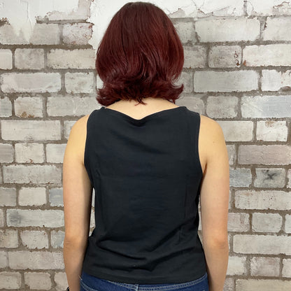 Person wearing a black sleeveless top against a brick wall.  Kings of Leon, Happy Cherry print graphic tshirt recycled by Unwantees, Upcycled Band tshirt by Unwantees, tank tops athleisure