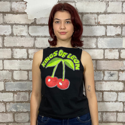 Person wearing a black sleeveless shirt with 'Kings of Leon' design against a brick wall.  Kings of Leon, Happy Cherry print graphic tshirt recycled by Unwantees, Upcycled Band tshirt by Unwantees, tank tops athleisure