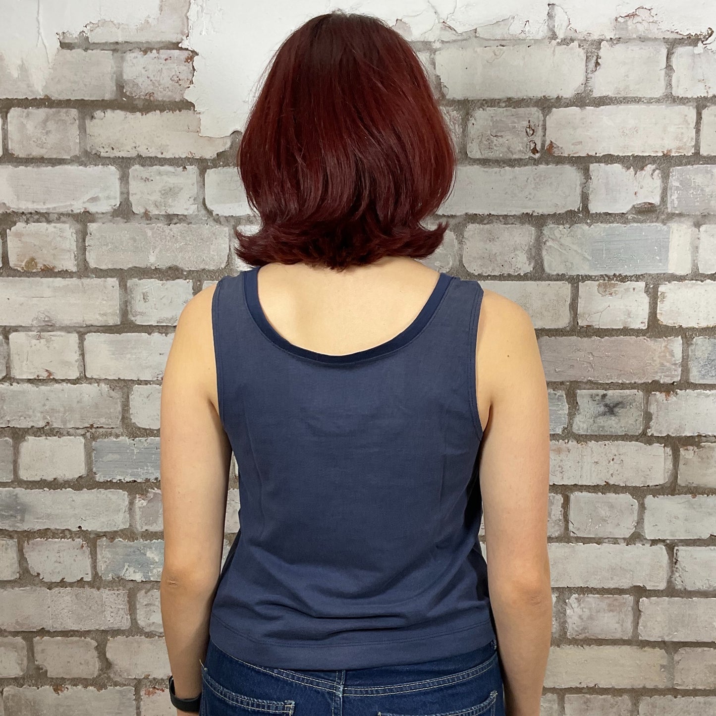 Person wearing a blue tank top standing against a brick wall.  One-of-a-kind Roanoke VA Mystical Night Sky graphic Scoop Neck Unwantee tank top front view, upcycled, sustainable, made in Britain