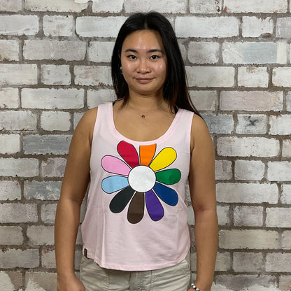 Person wearing a tank top with a colorful flower design against a brick wall.  One-of-a-kind Rainbow Flower graphic Scoop Neck Unwantee tank top front view, upcycled, sustainable, made in Britain