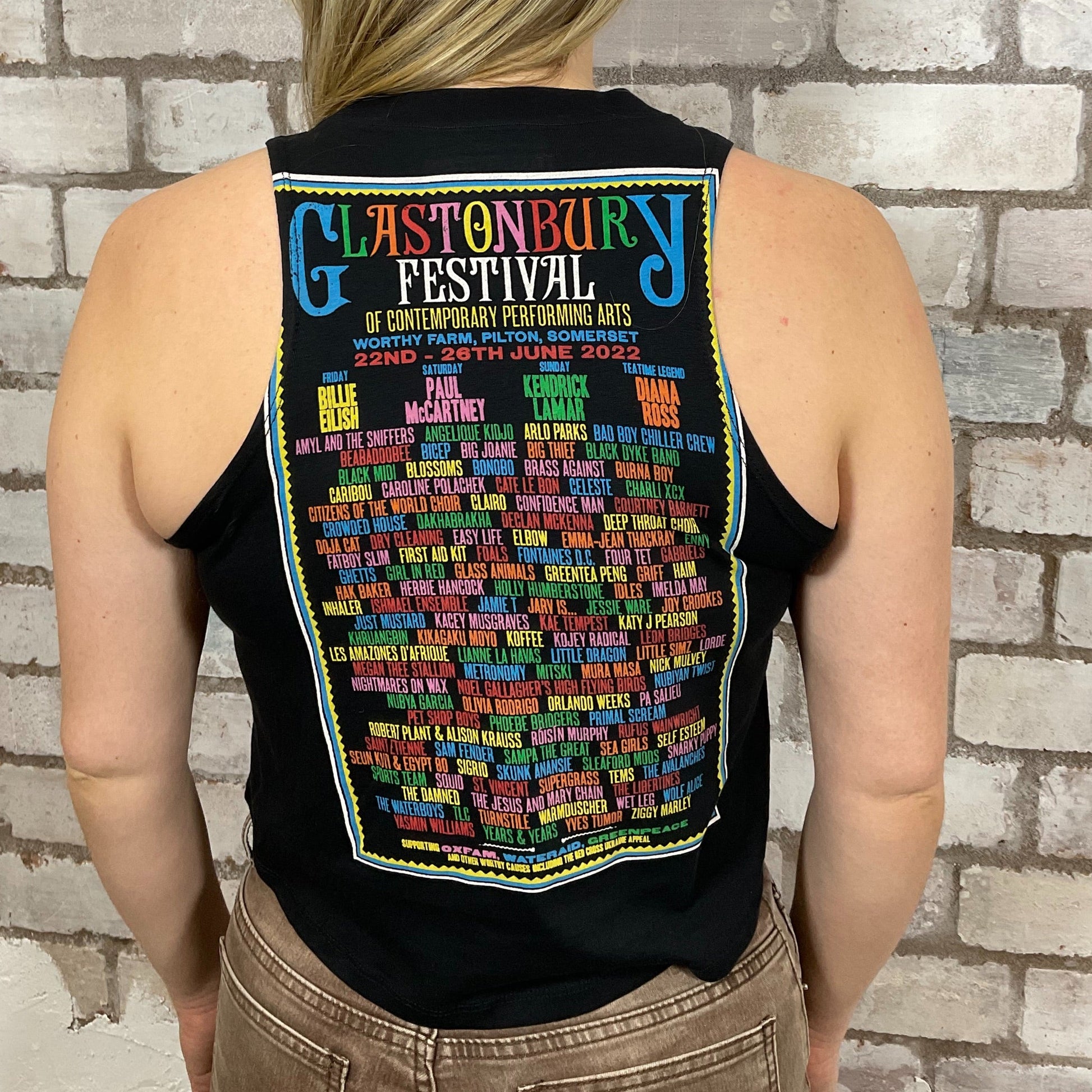 Glastonbury 2022 Legendary Artist Line Up including Billie Eilish, Elbow and Paul McCartney Official Merchandise Graphic print on 100% black cotton fabric, Unwantee made from upcycled and deconstructed graphic tshirt, punk rock style street wear, athleisure wear, unwantees is a sustainable fashion brand, we take unwanted graphic tshirts otherwise destined for landfill and recycle clothing into vest tops for sports wear or leisure.  Refashioned band merch, Slash Neck Sleeveless Top