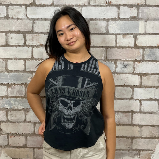 Person wearing a black sleeveless shirt with a skull design and text, standing against a brick wall.  One-of-a-kind Guns N’ Roses Skull in Top Hat graphic Racerback Unwantee tank top front view, upcycled, sustainable, made in Britain