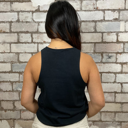 Person wearing a black sleeveless top against a brick wall.  One-of-a-kind Guns N’ Roses Skull in Top Hat graphic Racerback Unwantee tank top front view, upcycled, sustainable, made in Britain