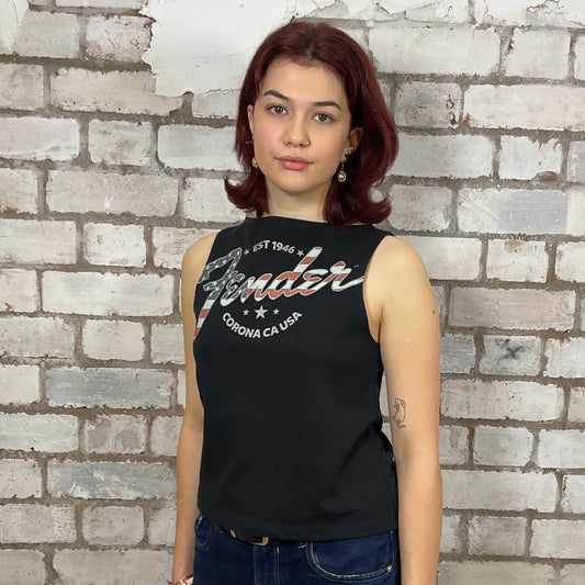 Woman wearing a black sleeveless shirt with branding against a brick wall.  Upcycled fender guitar tshirt by unwantees, recycled tank tops, one of a kind