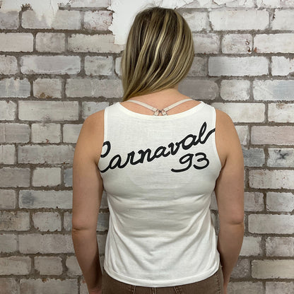 Person wearing a white tank top with 'Carnaval 93' text against a brick wall.  One-of-a-kind Rio Carnival 1993 graphic Slash Neck Unwantee tank top front view, upcycled, sustainable, made in Britain