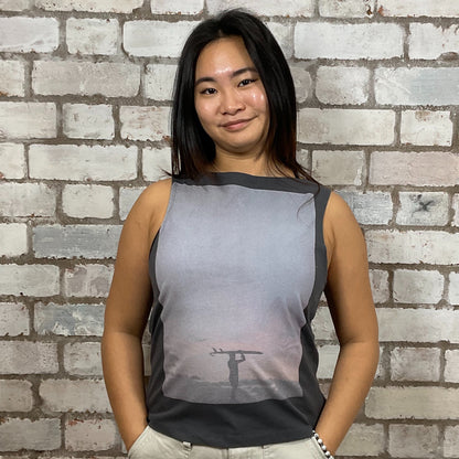 Person wearing a sleeveless shirt with a printed design against a brick wall.  Lone Surfer graphic tank top, surfing top, rip curl printed vest top upcycled tshirt by Unwantees