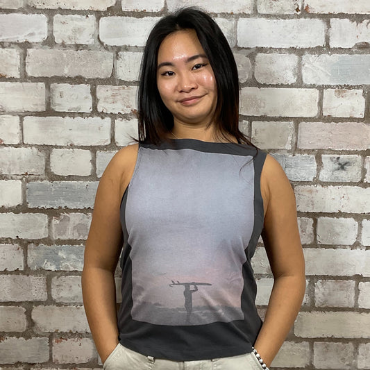 Person wearing a sleeveless shirt with a printed design against a brick wall.  Lone Surfer graphic tank top, surfing top, rip curl printed vest top upcycled tshirt by Unwantees