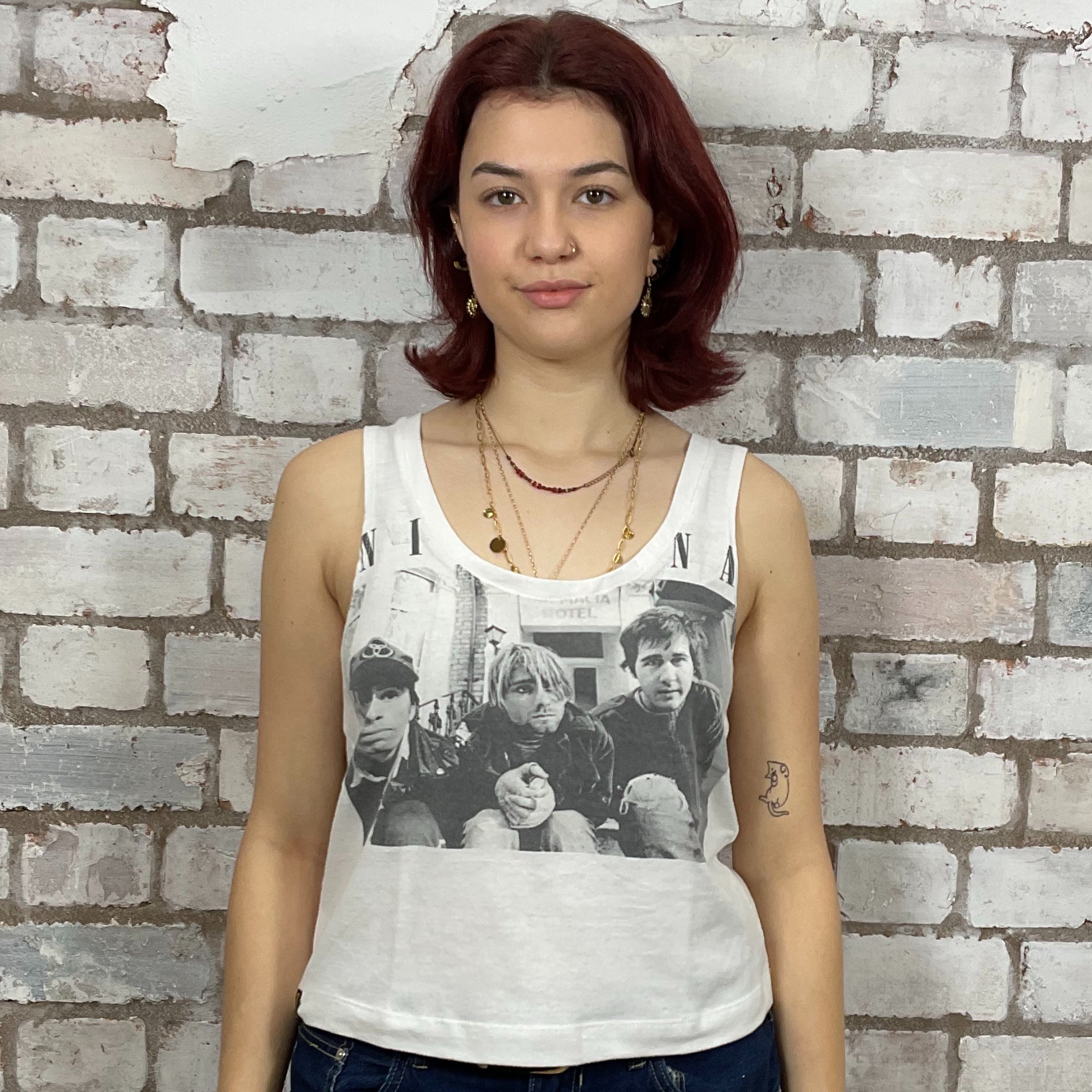 Person wearing a white tank top with Nirvana young band photo graphic design against a brick wall.