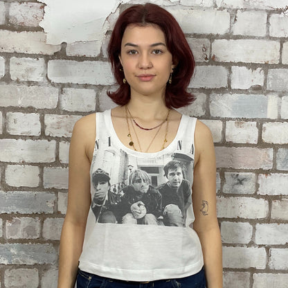 Person wearing a white tank top with Nirvana young band photo graphic design against a brick wall.