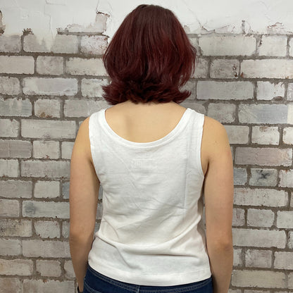 Person wearing a white tank top against a textured brick wall.  Person wearing a white tank top with Nirvana young band photo graphic design against a brick wall.