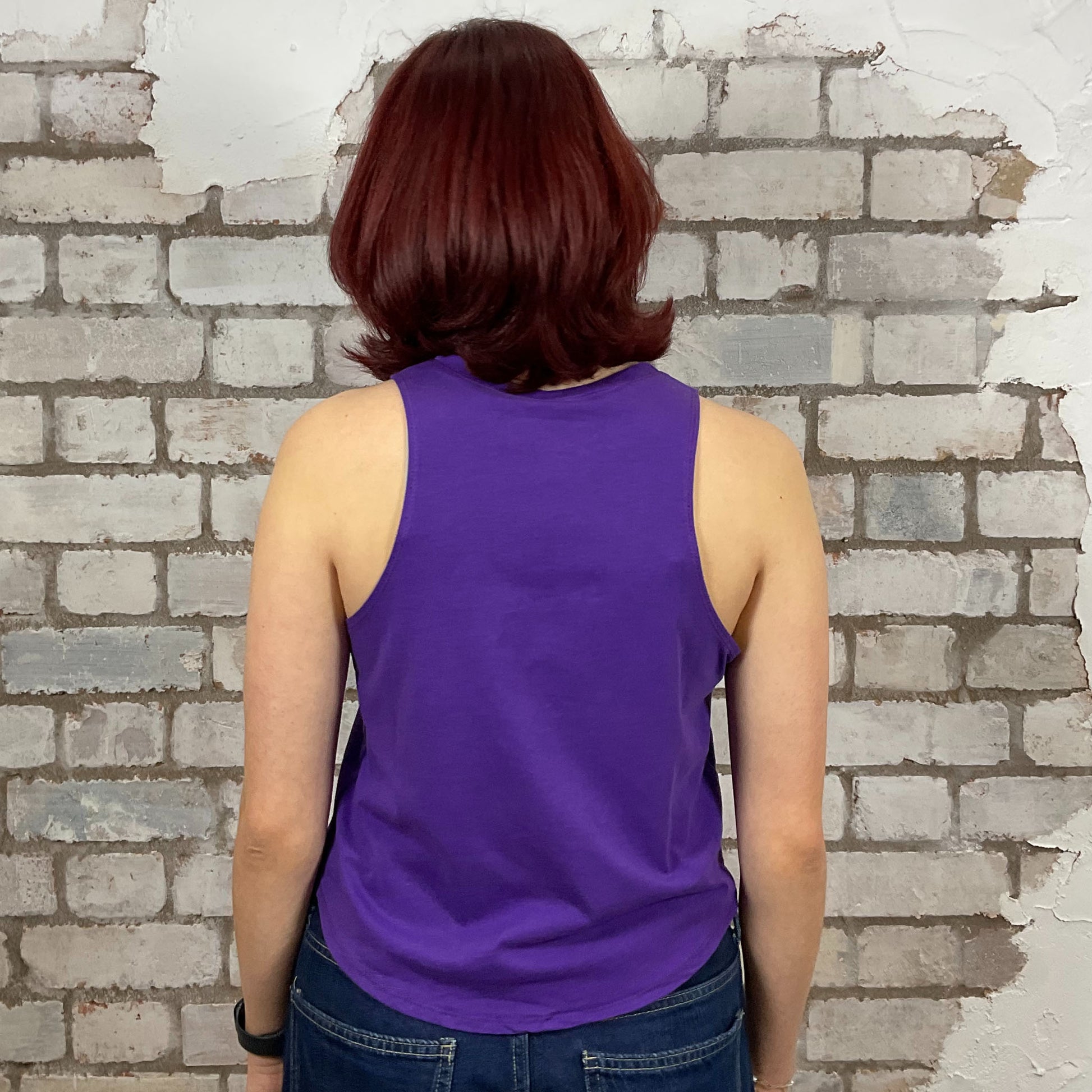Person wearing a purple tank top standing against a brick wall.  Lazy Varsity style tshirt upcycled by unwantees in the uk, one of a kind tank tops