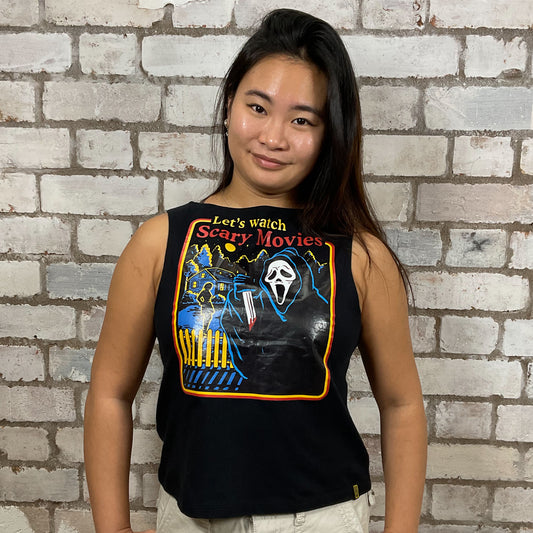 Person wearing a black tank top with a graphic design and text, standing against a brick wall.  One-of-a-kind Let's Watch Scary Movies graphic Slash Neck Unwantee tank top front view, upcycled, sustainable, made in Britain