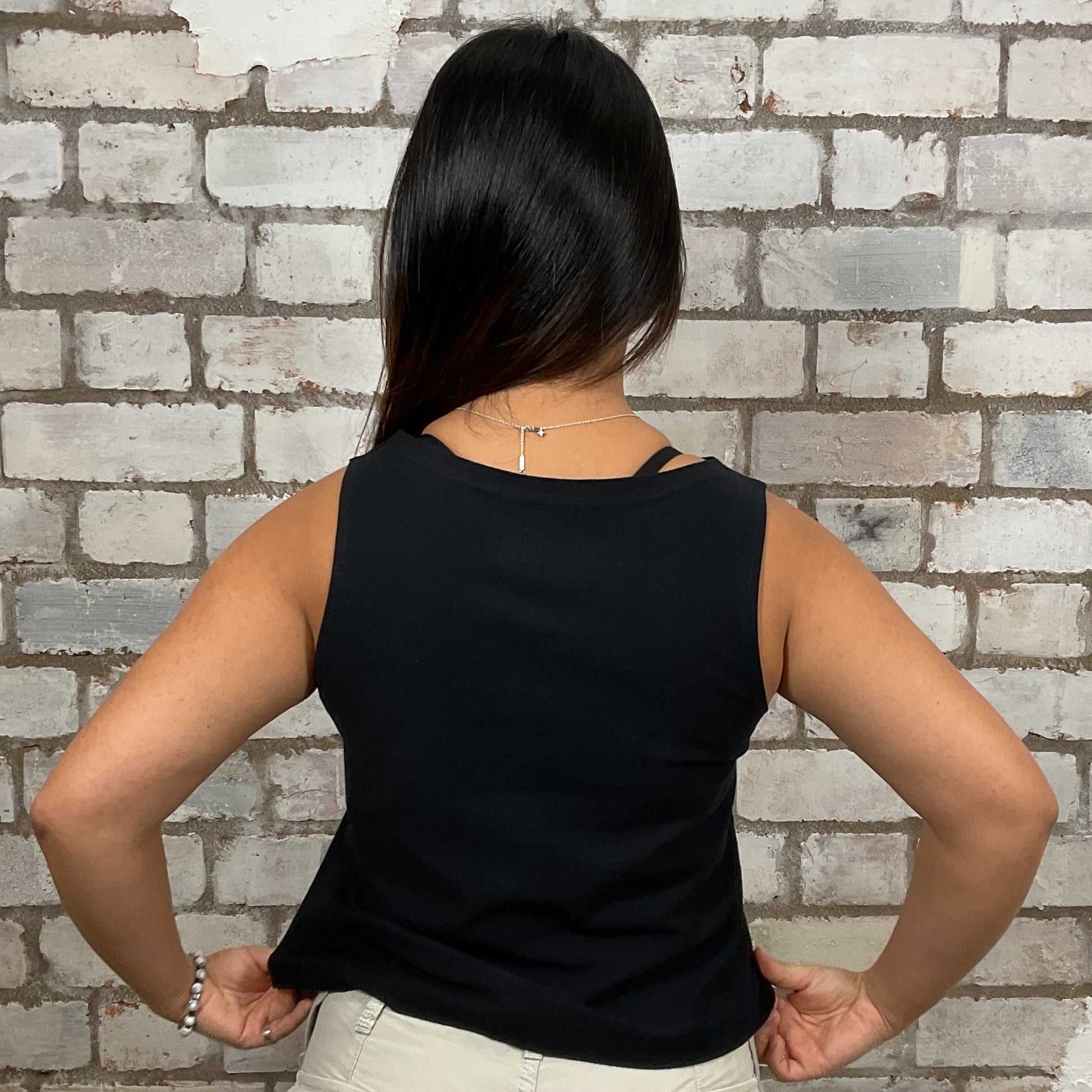 Person wearing a black sleeveless top against a brick wall.  v