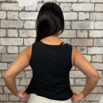 Person wearing a black sleeveless top against a brick wall.  v