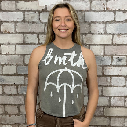 Person wearing a sleeveless shirt with 'bmth' and an umbrella graphic against a brick wall.  bmth Unwantees, Recycled clothing, sustainable fashion, athleisure wear, band tees, upcycled graphic tshirts, fashion recycled, Sustainable Fashion