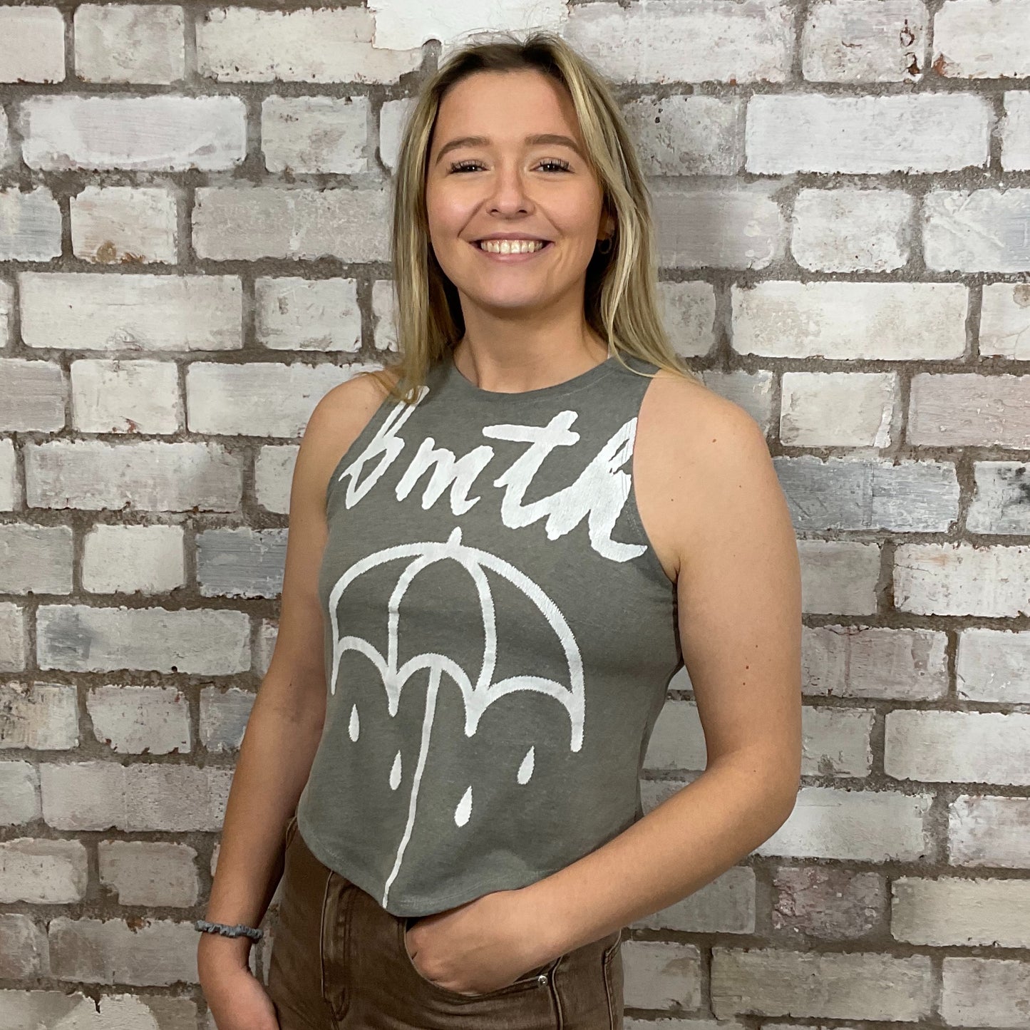 Woman wearing a sleeveless shirt with a graphic design against a brick wall.  bmth Unwantees, Recycled clothing, sustainable fashion, athleisure wear, band tees, upcycled graphic tshirts, fashion recycled, Sustainable Fashion