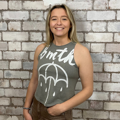 Woman wearing a sleeveless shirt with a graphic design against a brick wall.  bmth Unwantees, Recycled clothing, sustainable fashion, athleisure wear, band tees, upcycled graphic tshirts, fashion recycled, Sustainable Fashion