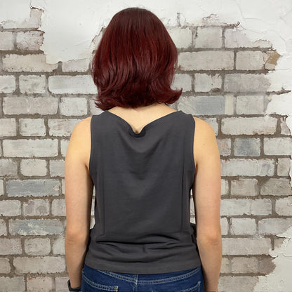 Person wearing a dark gray sleeveless top with a brick wall background.  One-of-a-kind Fleetwood Mac graphic Slash Neck Unwantee tank top front view, upcycled, sustainable, made in Britain