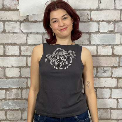 Person wearing a black sleeveless shirt with 'Fleetwood Mac' logo against a brick wall.  One-of-a-kind Fleetwood Mac graphic Slash Neck Unwantee tank top front view, upcycled, sustainable, made in Britain