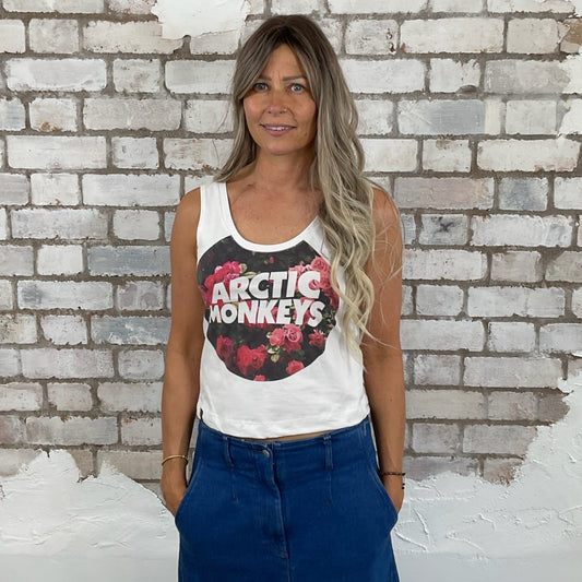 Woman wearing a white tank top with Arctic Monkeys logo in front of a textured brick wall.  Arctic Monkeys Floral Tank Top, Vibrant coloured top by Arctic Monkeys Up Cycled recycled by Unwantees
