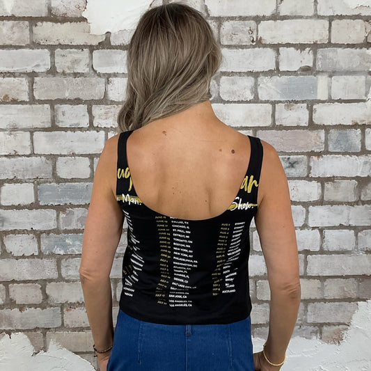 Person wearing a black tank top with yellow text against a white brick wall.