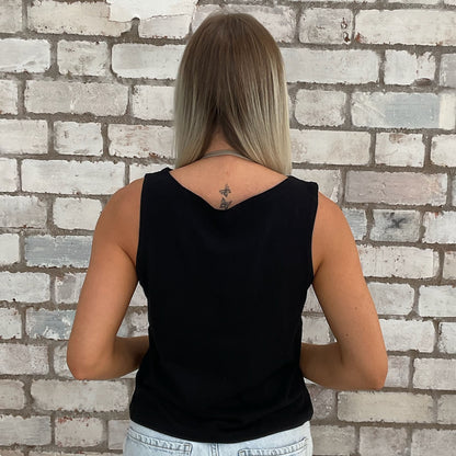 Person wearing a black sleeveless top against a brick wall.