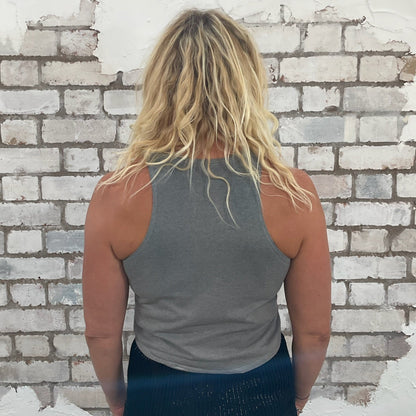Person wearing a grey tank top and blue shorts standing against a textured brick wall.  bmth Unwantees, Recycled clothing, sustainable fashion, athleisure wear, band tees, upcycled graphic tshirts, fashion recycled, bring me the horizon band top